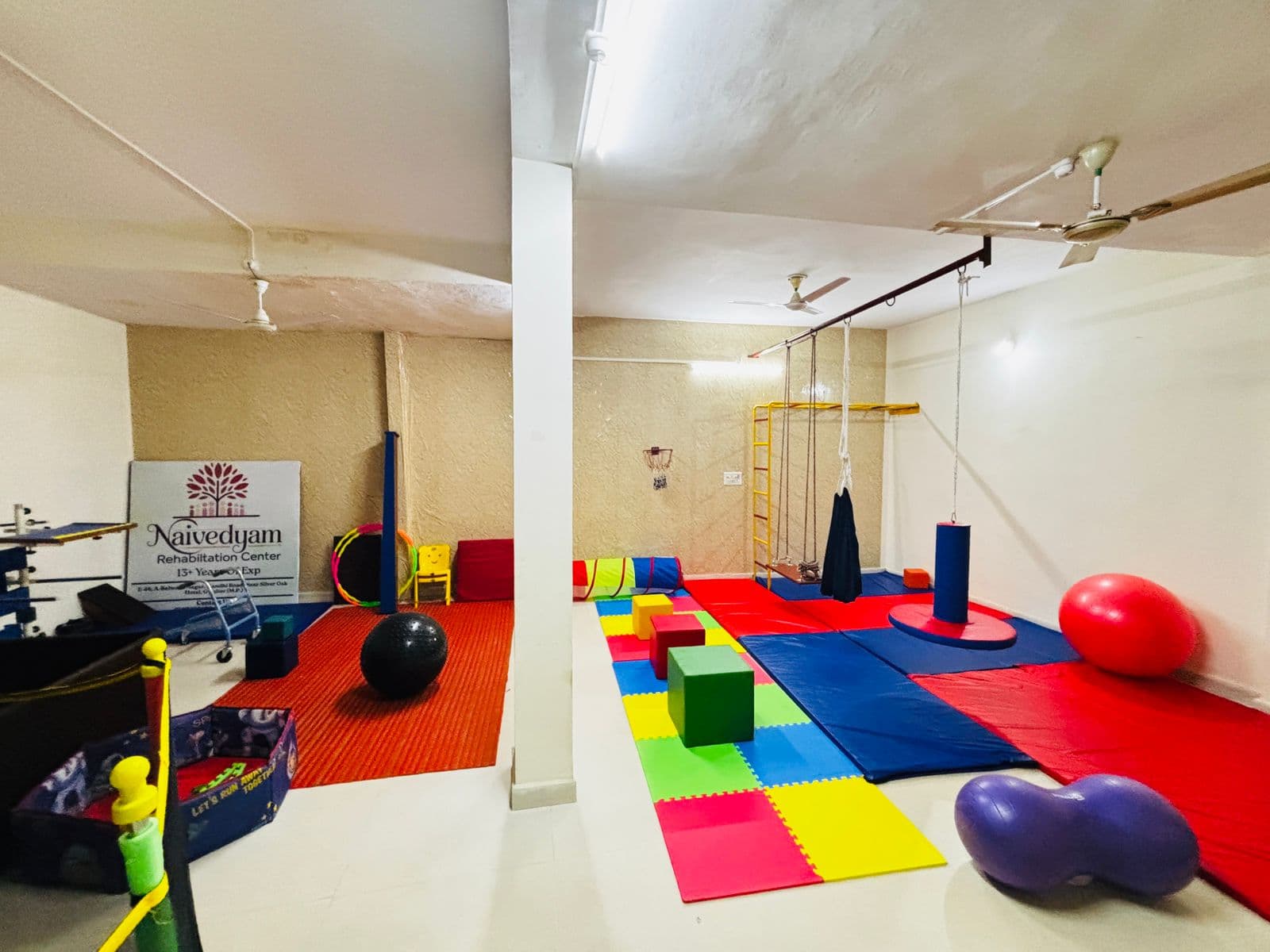 Main therapy hall at Naivedyam with mats, swings, and the center signage on the wall